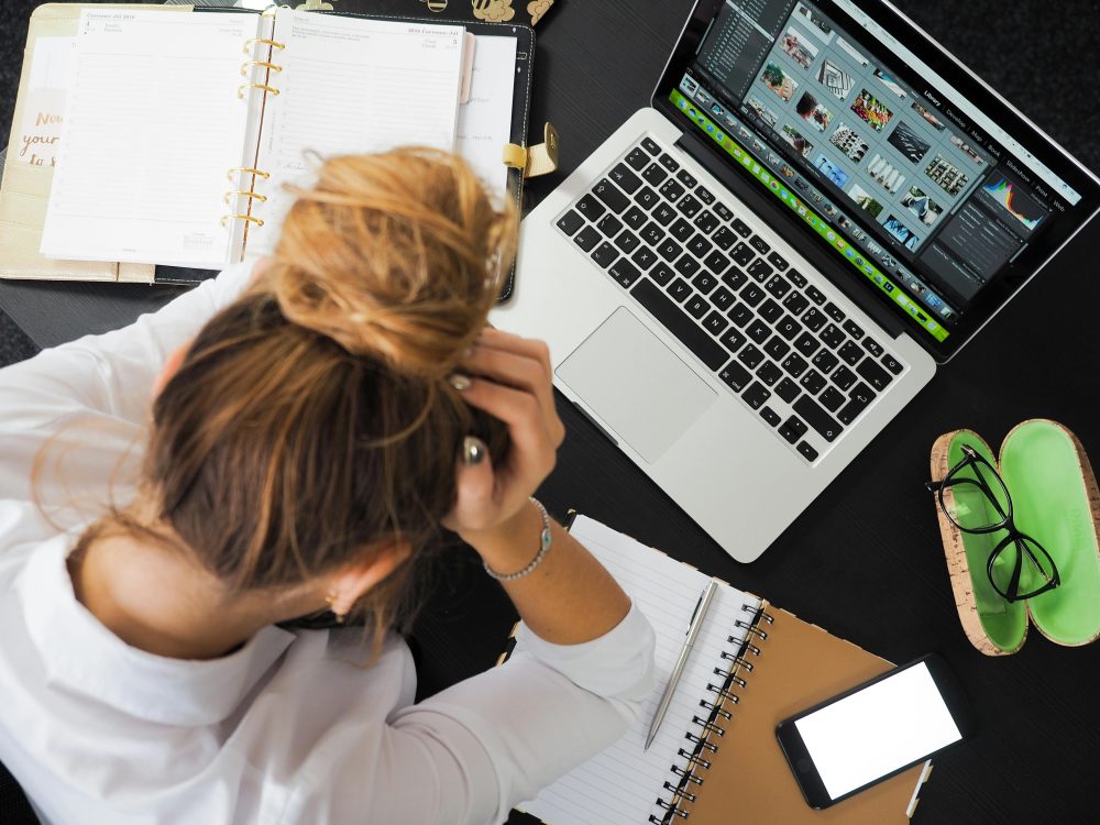 women working on a computer holding her head