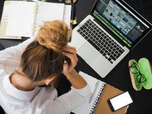 women working on a computer holding her head